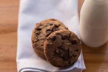 Stack of chocolate chips cookies and a bottle of milk on wooden background