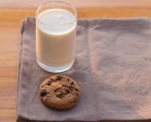 chocolate chips cookie and a glass of milk on brown background