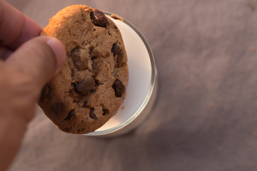 chocolate chips cookie and a glass of milk on brown background