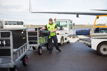 Male Worker Placing Luggage In Trailer On Runway