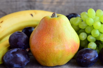 Fresh colorful fruits assortment. Fresh raw pear, grapes, blue plums, bananas on a wooden table. Closeup