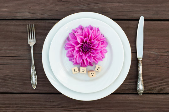 Aster flower on a plate with a box of jewelry present, next to a silver fork and knife. 