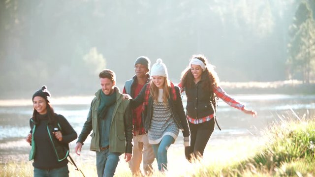 Five friends on a camping trip walking in a row near a lake