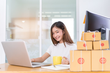 Young asian woman freelancer small business private working at home office with laptop, note, coffee, packaging delivery online market on purchase orders to customer.