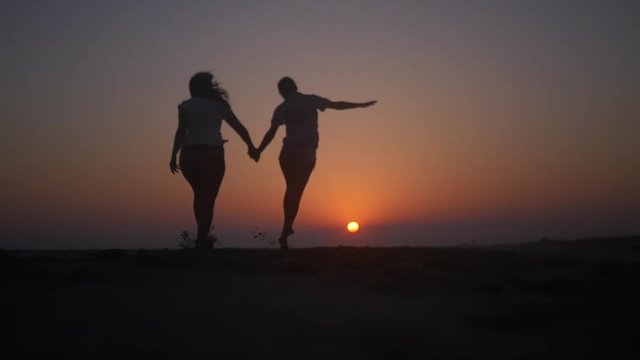 Joyfully jumping at sunset on the beach holding hands. HD, 1920x1080. slow motion.