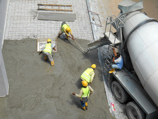 Construction workers leveling wet concrete has been poured. They also use a vibrator machine in this work.