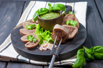 Boiled beef tongue on dark wooden table with pesto and salad
