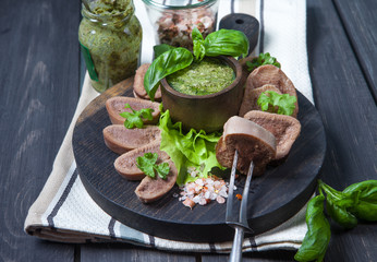 Boiled beef tongue on dark wooden table with pesto and salad