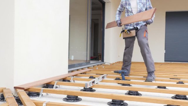 handsome young man carpenter installing a wood floor outdoor terrace in new house construction site