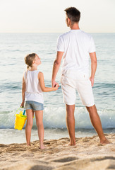 father with daughter standing back forward on sandy beach on vacation
