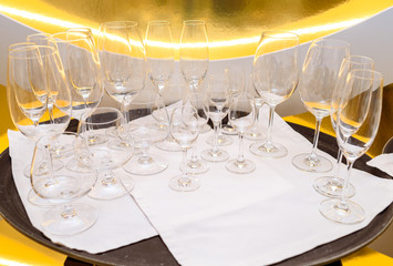 Close up of many empty glasses on tray in restaurant with gold background, free space. Crystal glasses ready for celebration on table. Champagne, wine, cognac glasses at luxury wedding reception