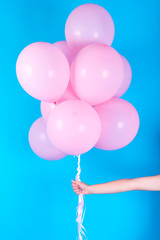 Girl hand holding pink air balloons on blue background, free space. Pink birthday balloons. Concept of love, happiness, birthday, valentine. Happy holiday pink balloons