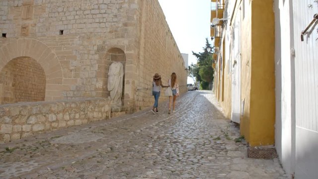 Two female friends walking through old Ibiza, back view