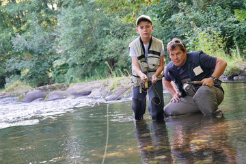 Father teaching son how to fly-fish in river