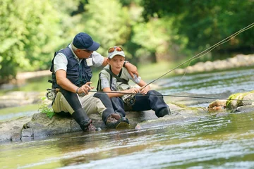 Tuinposter Father and son fly-fishing in river, sitting on rocks © goodluz