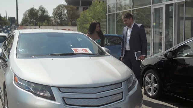 Woman talks with salesman and find out details of buying auto in car dealership