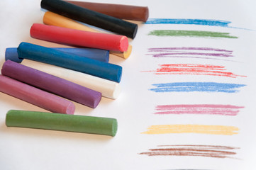 Fototapeta premium A set of multicolored pastel pencils on a light background with a trail drawn next to it. Selective focus