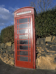 Obraz premium Traditional red telephone kiosk built into brick wall with blue sky