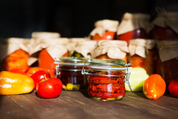 Sun dried tomatoes with olive oil in a jar. Preserved and fresh vegetables on home table. Various homemade conserves in glass jars 