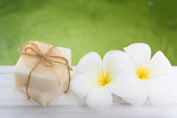 Spa milk soap and Frangipani flowers on white wood table with green pond background