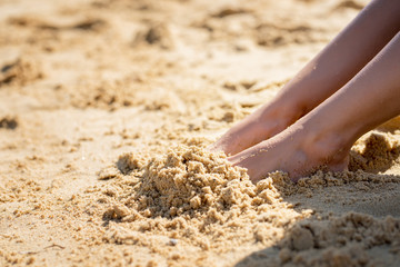 Picture of female feet buried in sand at the beach.