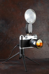 A vintage lamp made from an old film camera on a brown cement background.
