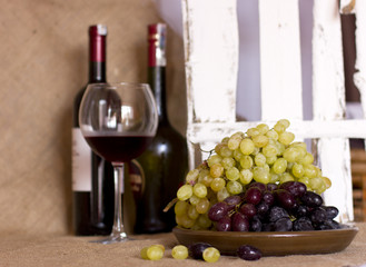 Obraz premium Blue and green grapes on a clay brown dish. Bottle with red and white wine on background