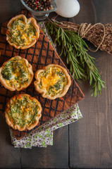 Savory mini quiches (tarts) on a wooden board. Flaky dough pies. Fresh rosemary and dry thyme on a wooden background. - 172976312