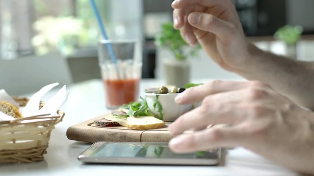 Man eating olives and cheese in the cafe while texting on smartphone, steadycam shot
