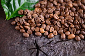 Coffee beans and green leaves of coffee plant on an old wooden desk. Top view of coffee beans with a copy space for your text. Natural coffee background.