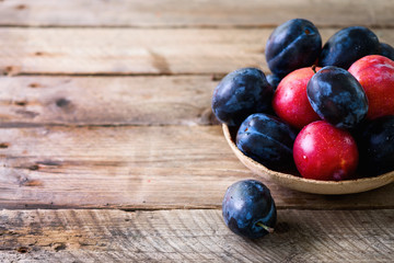 Blue and pink organic plums on dark wooden background. Copyspace.