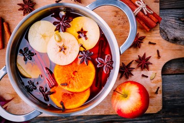 Hot mulled wine drink with citrus, apples, cinnamon sticks, cloves and anise in cooking pan