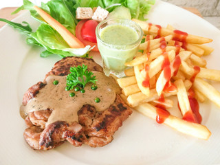 Grilled t-bone  steak seasoned withand served with golden French fries, fresh leafy herb salad and a tomato