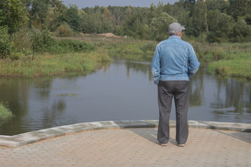 Fototapeta premium An elderly man stands on a bridge and looks at the river 