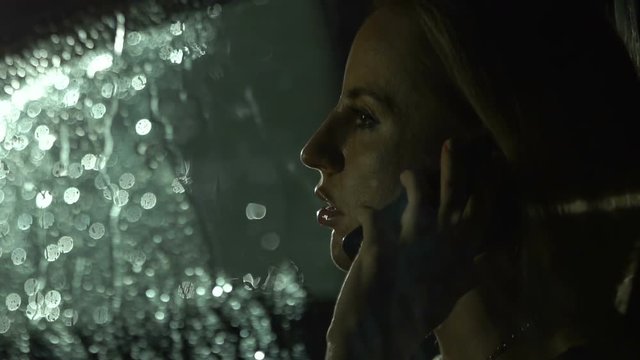 Portrait of woman talking on phone in the car. Rain at the night. Emergency call.