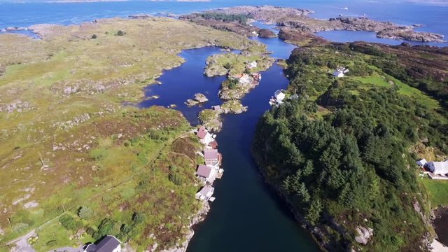 Islands are covered with green plants in the middle of the blue clear sea. Norway, Europe. View from above of a small settlement near the coastline. Beautiful nature, small private suburban houses