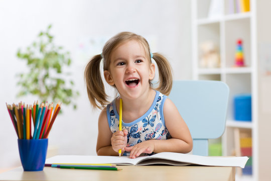 Expressive kid girl draws sitting at table in room in nursery