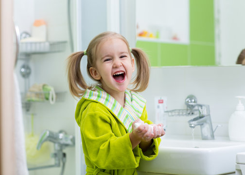 Smiling child little girl washing hands in bathroom