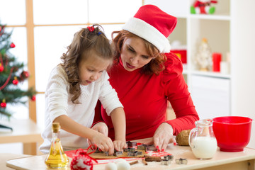 Happy woman and child girl cutting the christmas cookies out of dough together