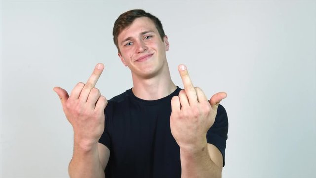 Portrait of a young man showing middle finger gesturing fuck on white background. White man makes fuck gesture with a hand on light gray background