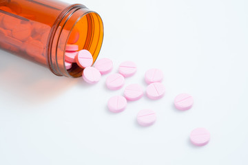 Pink pills an pill bottle on white background