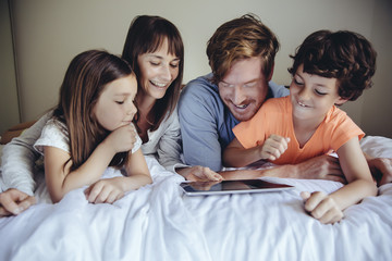 Children and their parents looking at tablet on bed