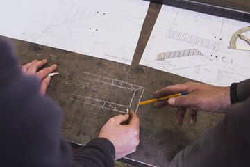 Two blacksmiths are taking measures, do calculations and schedule a days work in a blacksmith's workshop.
