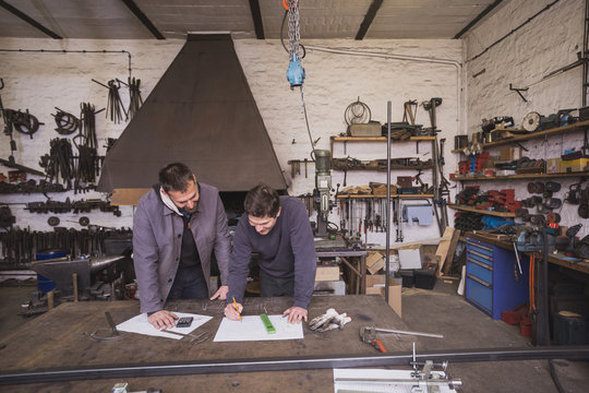 Two blacksmiths are taking measures, do calculations and schedule a days work in a blacksmith's workshop.