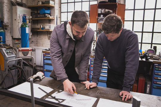 Two blacksmiths are taking measures, do calculations and schedule a days work in a blacksmith's workshop.