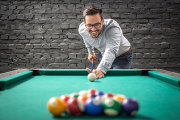 Happy businessman playing a game of billiards and preparing to break pyramid of balls on the table.