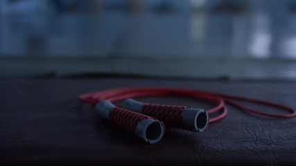 Red jump rope with black handles on a black gym floor, closeup