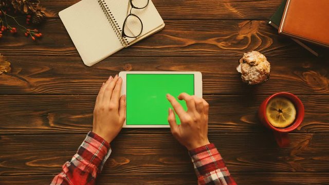 Autumn concept flat lay. Woman using tablet device with green screen in horizontal position on the wooden table. Top view. Chroma key