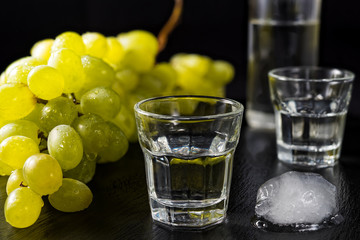 Glasses and  bottle of traditional drink Ouzo or Raki on black dish with a branch of grapes