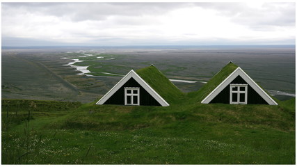Two wooden cabins with grass roofs and a view of icelandic nature in the background